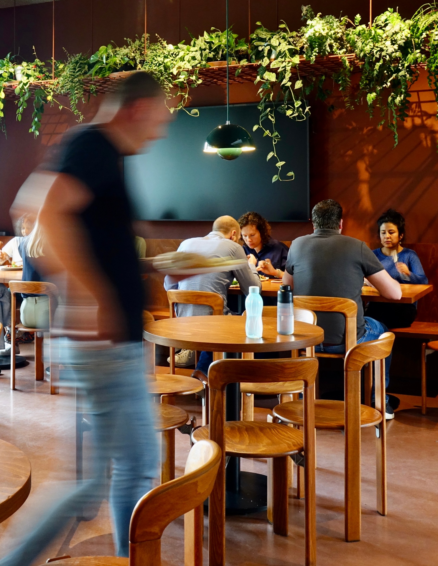 Cafetaria met hangende planten en mensen aan tafel
